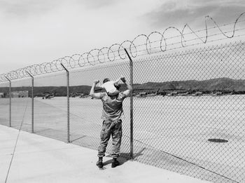 Rear view full length of soldier carrying child by fence at marine corps base camp pendleton