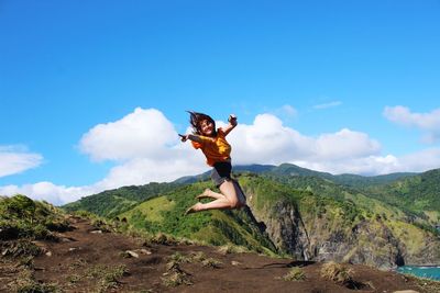 Mid adult woman jumping on mountain against blue sky during sunny day