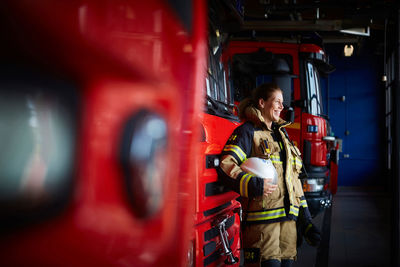 Smiling female firefighter standing by fire engine at fire station