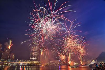 Low angle view of firework display over river against sky