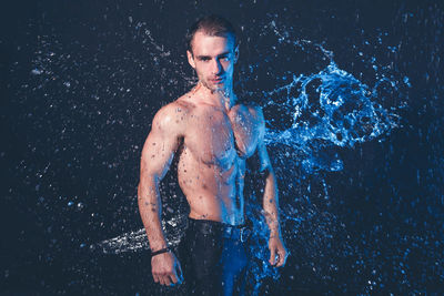 Portrait of shirtless man standing against black background