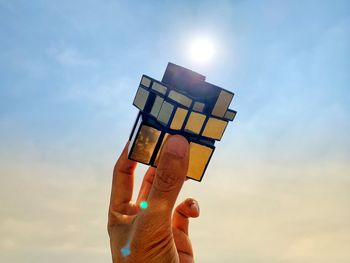 Low angle view of person holding puzzle cube against sky