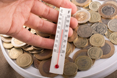 Close-up of hand holding thermometer above coins 
