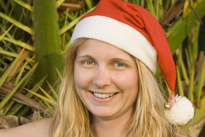 Close-up portrait of happy woman wearing santa hat against plants