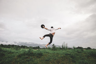 Man jumping on field against sky