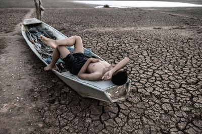 Full length of boy lying on boat over cracked land