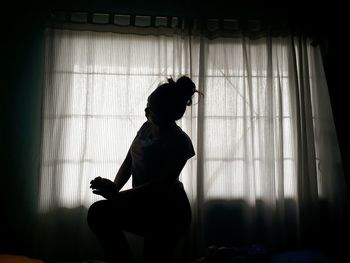 Woman kneeling on bed by window at home