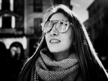 Close-up of smiling young woman wearing sunglasses while standing against buildings