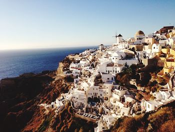 Buildings on cliff by sea against clear sky at santorini