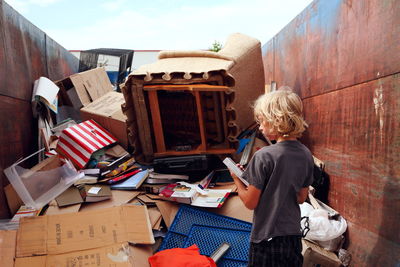 Rear view of boy standing by abandoned objects in dumpster