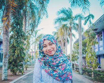 Portrait of smiling young woman standing against palm trees