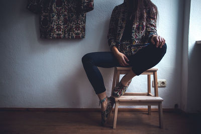Low section of woman sitting on stool against wall