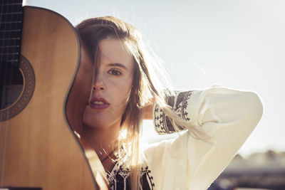 Close-up portrait of young woman by guitar against clear sky