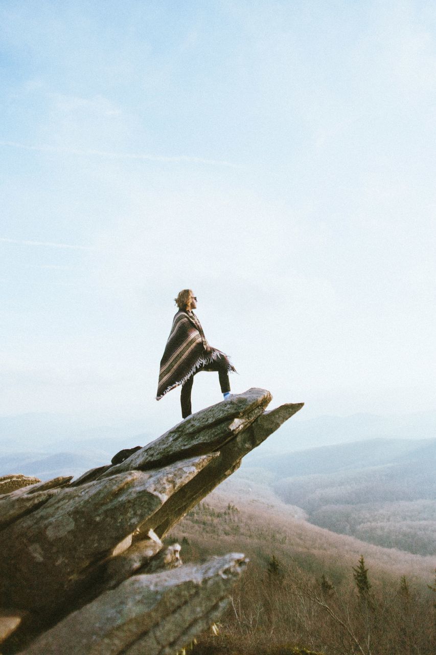 LOW ANGLE VIEW OF MAN STANDING ON MOUNTAIN