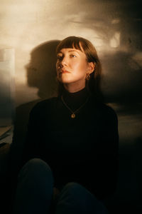 Portrait of a young woman sitting against wall