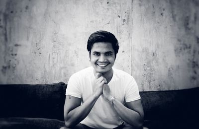 Portrait of smiling young man sitting against wall