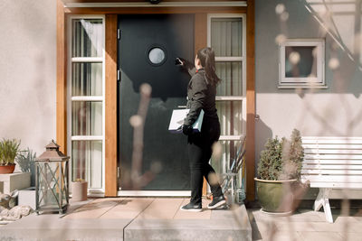 Young delivery woman with package at entrance of house