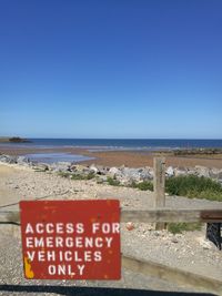 Information sign on beach against clear blue sky