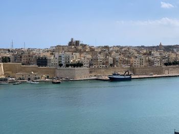 Sea by buildings in city against sky