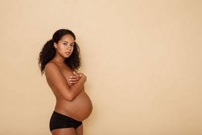 Portrait of shirtless pregnant woman standing against white background