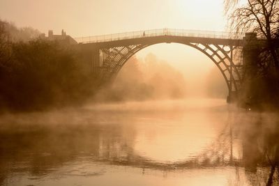 Arch bridge over river during sunset