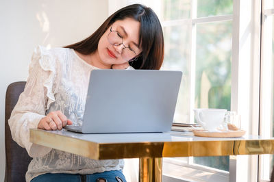 Young woman using mobile phone while sitting on table