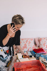 Side view of young woman using mobile phone while sitting on bed at home