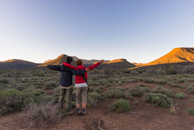 Couple standing on landscape against blue sky