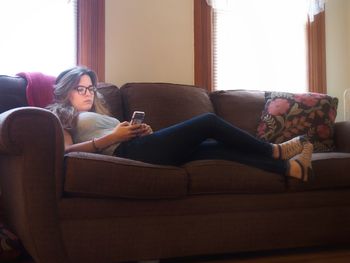 Side view of young woman relaxing on sofa at home