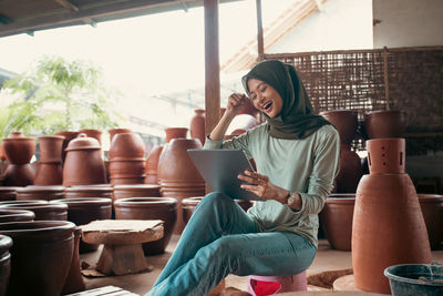 Smiling woman in hijab using digital tablet at work shop