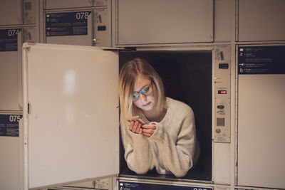 Young woman using phone in locker