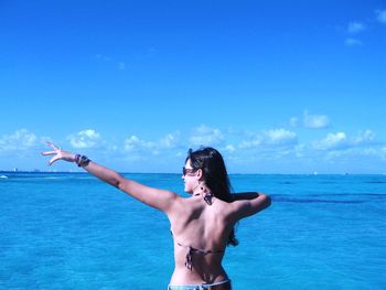 Rear view of woman with arms outstretched while standing by sea against sky