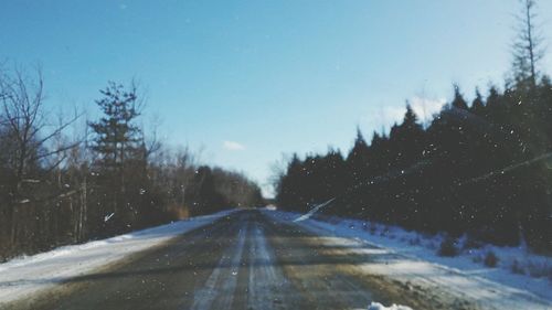 Road amidst bare trees against clear sky during winter