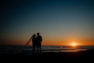 Silhouette men on beach against sky during sunset