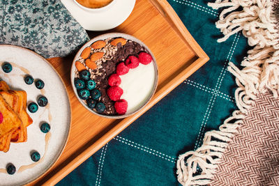 Cozy breakfast in bed from above, yogurt bowl with berries and nuts, french toasts, on wooden plate