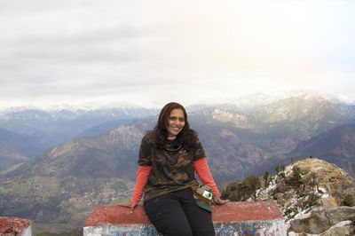 Woman traveler sitting outside kartik swami temple and looking at camera and mountain range