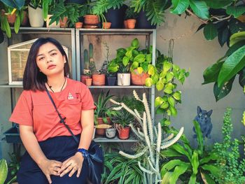 Portrait of young woman sitting against potted plants