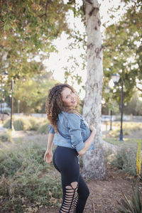 Side view of young woman standing against trees