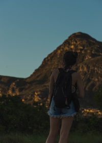 Rear view of man standing on rock against sky