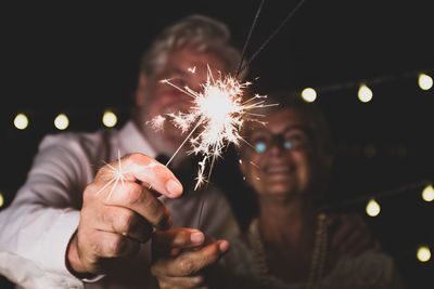 Senior couple holding sparklers standing outdoors at night