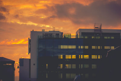 Buildings in city against dramatic sky during sunset