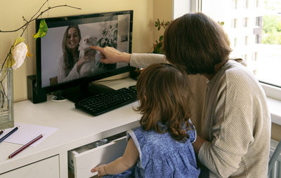 Mother with daughter video conferencing over computer at home