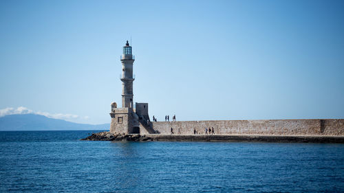 Lighthouse by sea against blue sky