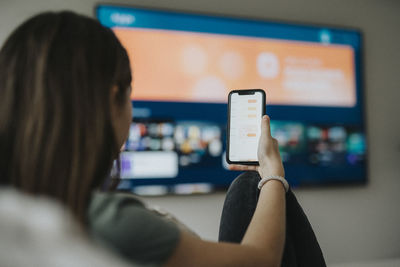 Girl using smart phone app while watching tv in living room at home