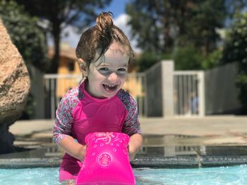 Portrait of cheerful girl holding water wings while standing in swimming pool