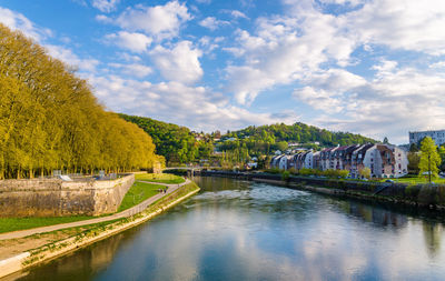 Arch bridge over river amidst trees and buildings against sky