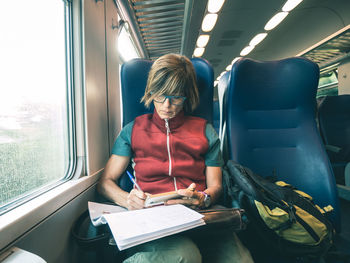 Woman writing on book while traveling in train
