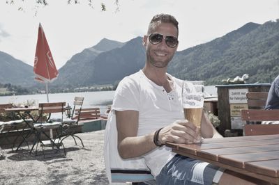 Young man holding beer at table against mountains