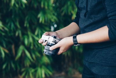 Midsection of man holding camera against tree