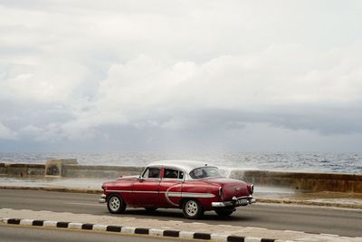 Vintage car on road by sea against sky